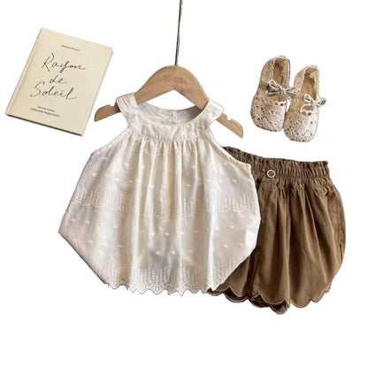 Children's white dress and brown shorts on a wooden table with a book and shoes.