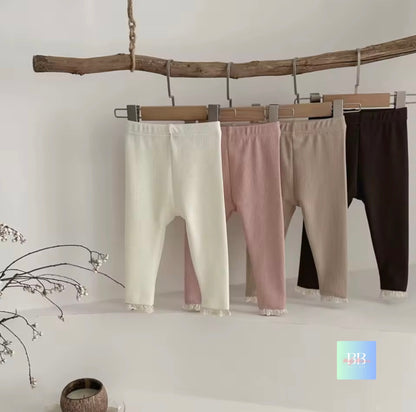 Three pairs of leggings in white, pink, and black hanging on a wooden branch against a white wall.