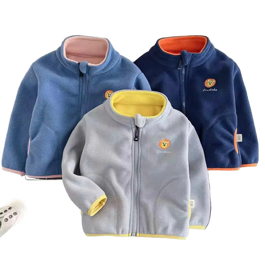 Three children's fleece jackets in blue, gray, and navy on a textured surface with shoes and a teddy bear.