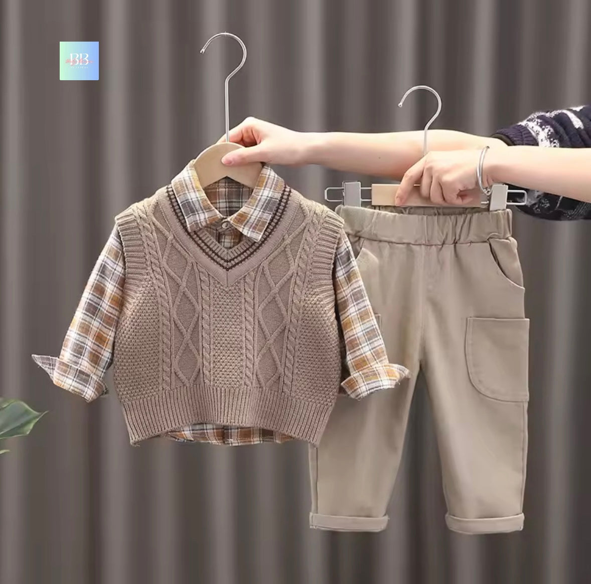 Children's clothing set with sweater vest and pants on hangers against a neutral background