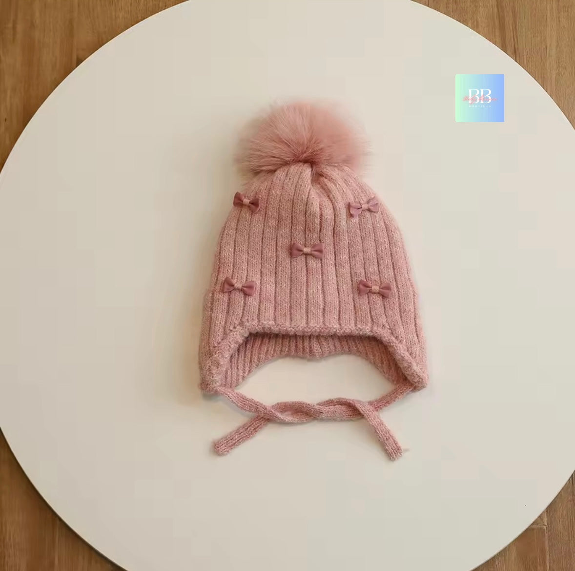 Pink knitted baby hat with a pom-pom on a white surface