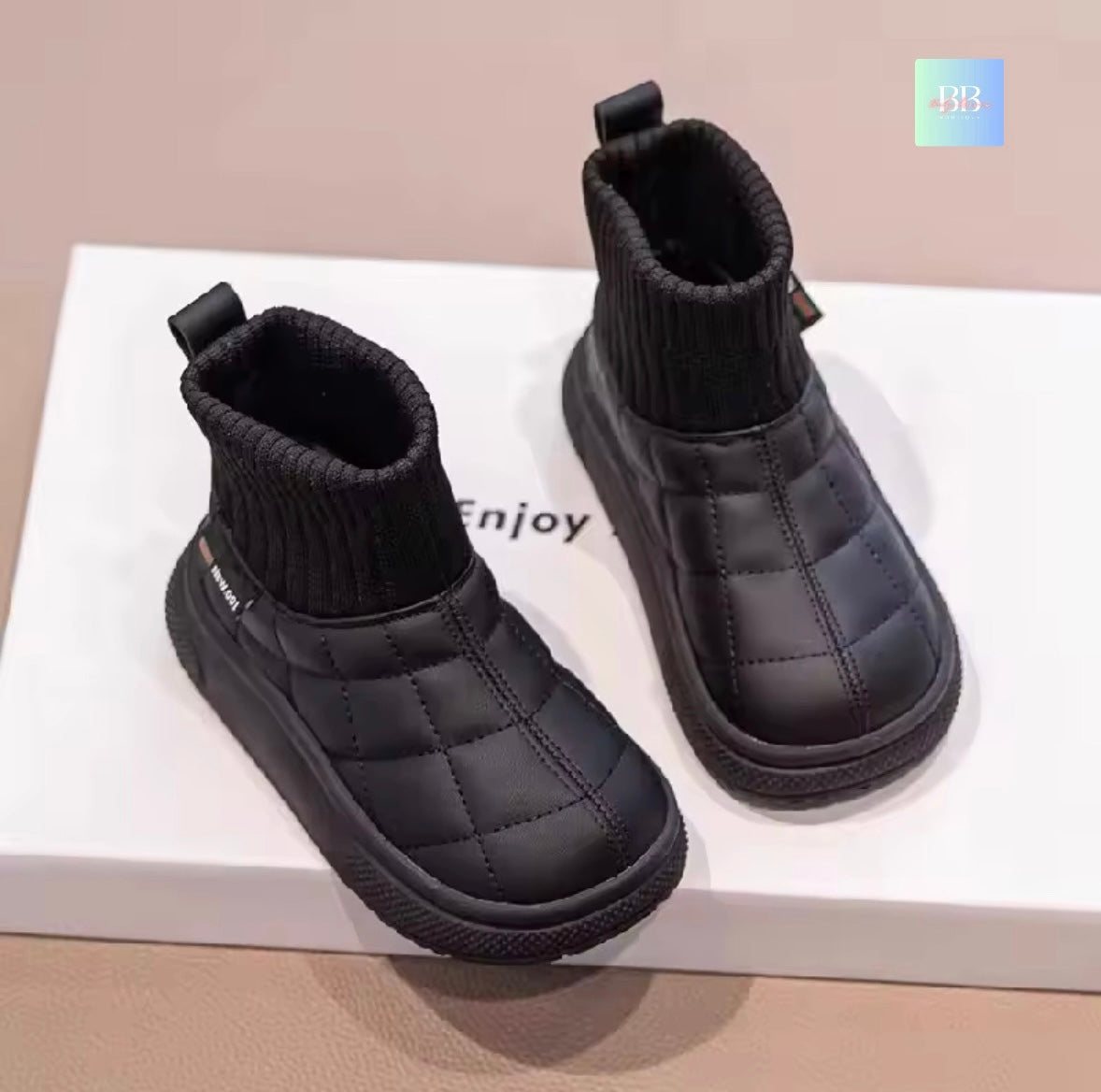 Pair of black quilted ankle boots on a white surface with 'Enjoy' text.