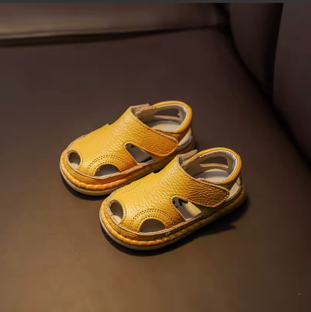 Pair of yellow children's sandals on a dark surface