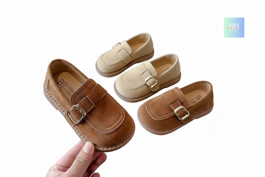 Pair of brown and beige children's loafers on a white surface with a hand holding one shoe.