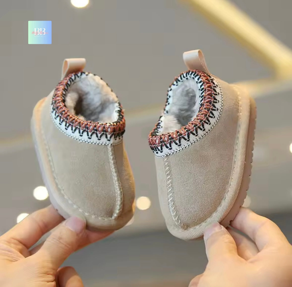 Beige baby shoes with decorative sole held by hands against a blurred background
