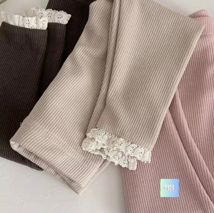 Three pairs of ribbed leggings with lace trim in black, beige, and pink on a light background.