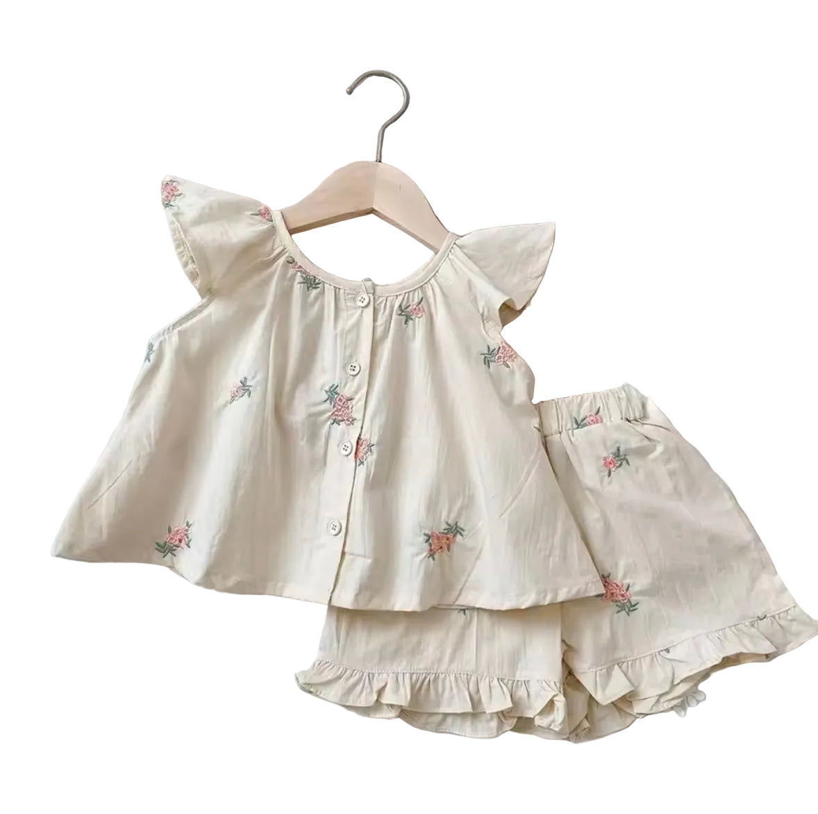 Children's outfit with top and shorts on a hanger, straw hat, and tote bag on a textured surface.