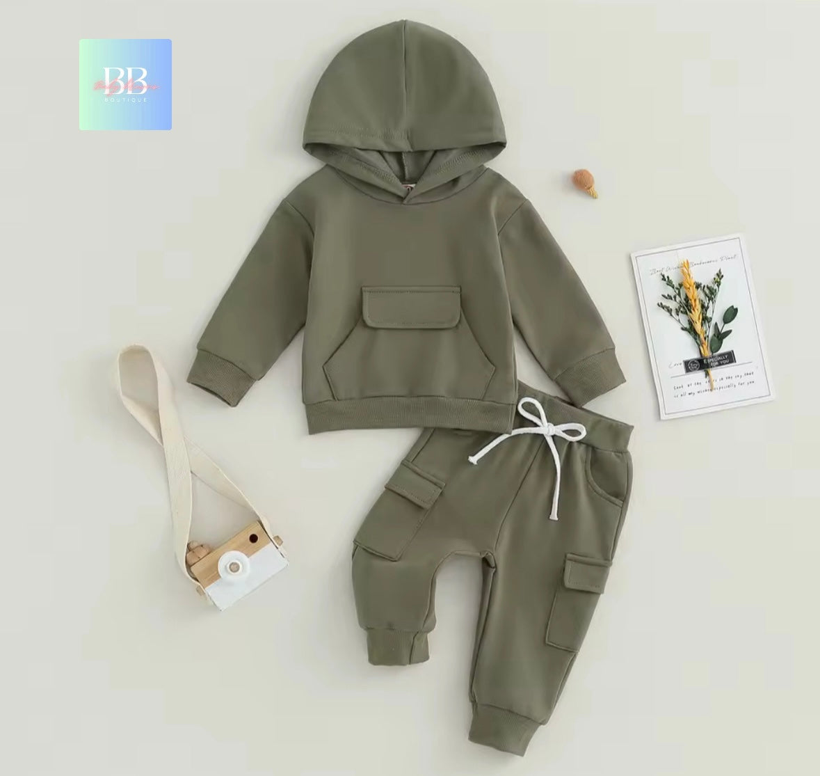 Green hoodie and pants set on a light gray background with a plant-themed card and strap.