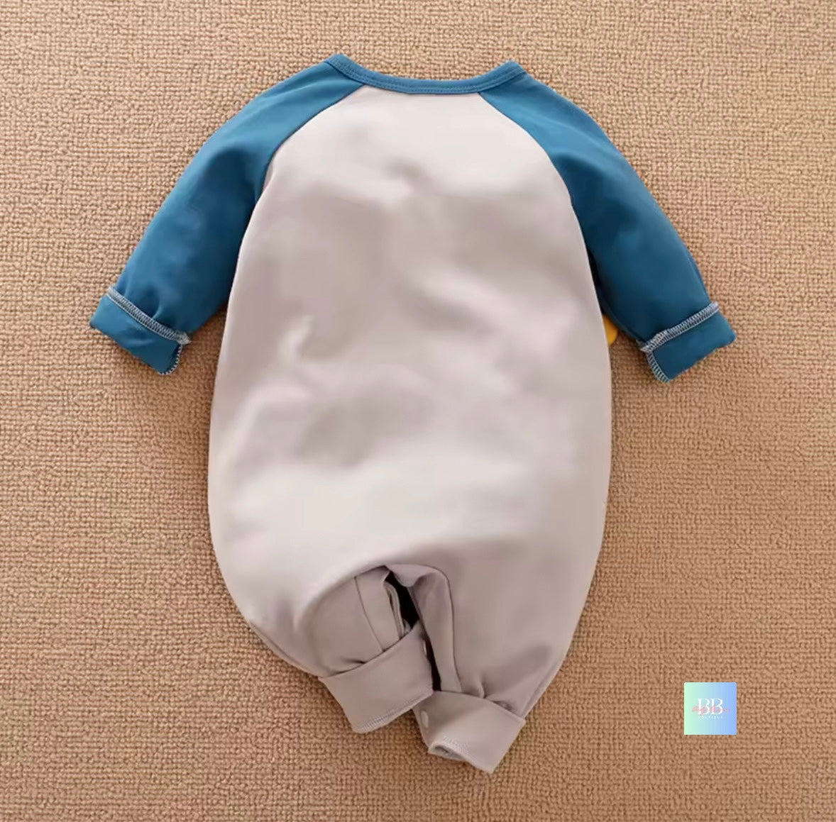 Baby romper with blue sleeves on a beige textured surface