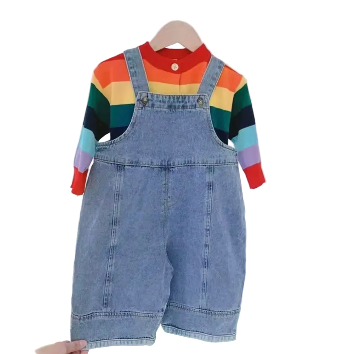 Denim overalls worn with a colorful striped shirt on a hanger against a white brick wall.