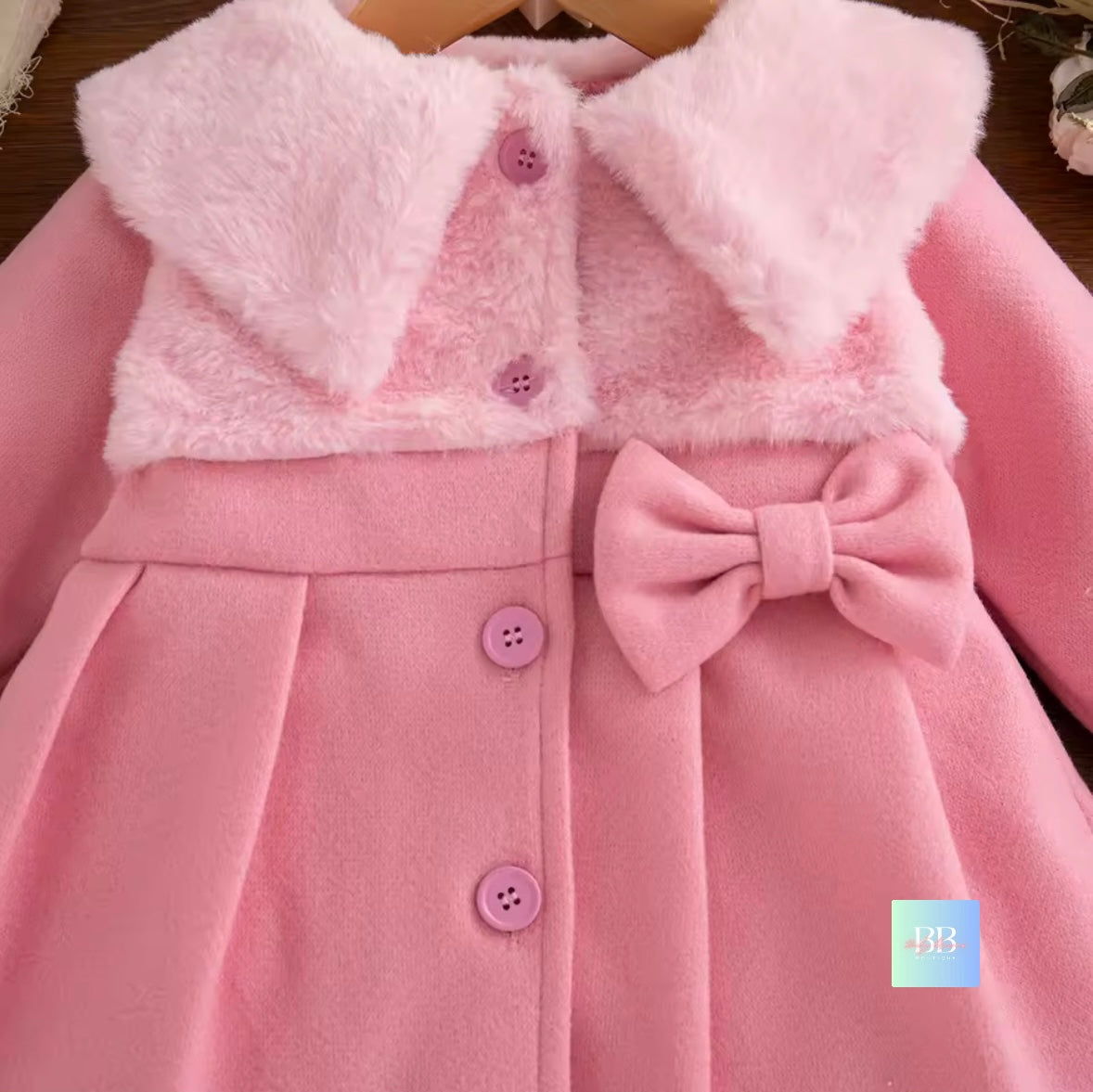 Pink children's coat with a bow detail on a wooden surface