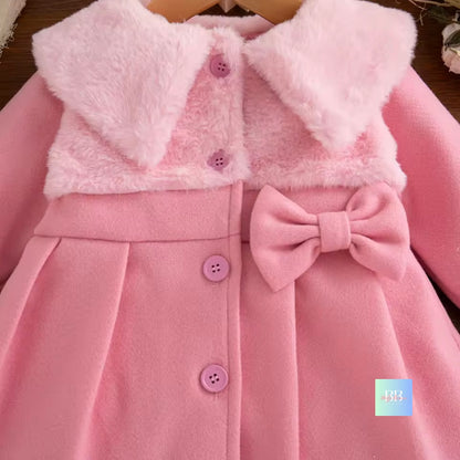 Pink children's coat with a bow detail on a wooden surface