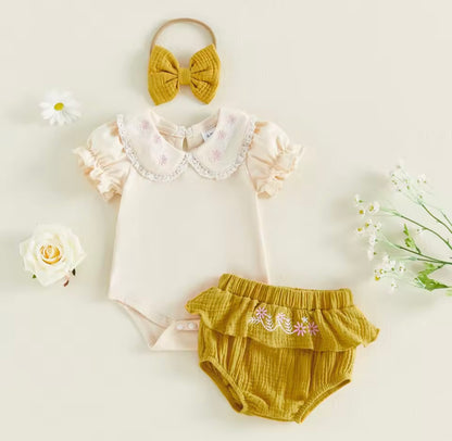 Baby outfit set with white bodysuit, mustard bloomers, and headband on a light background.
