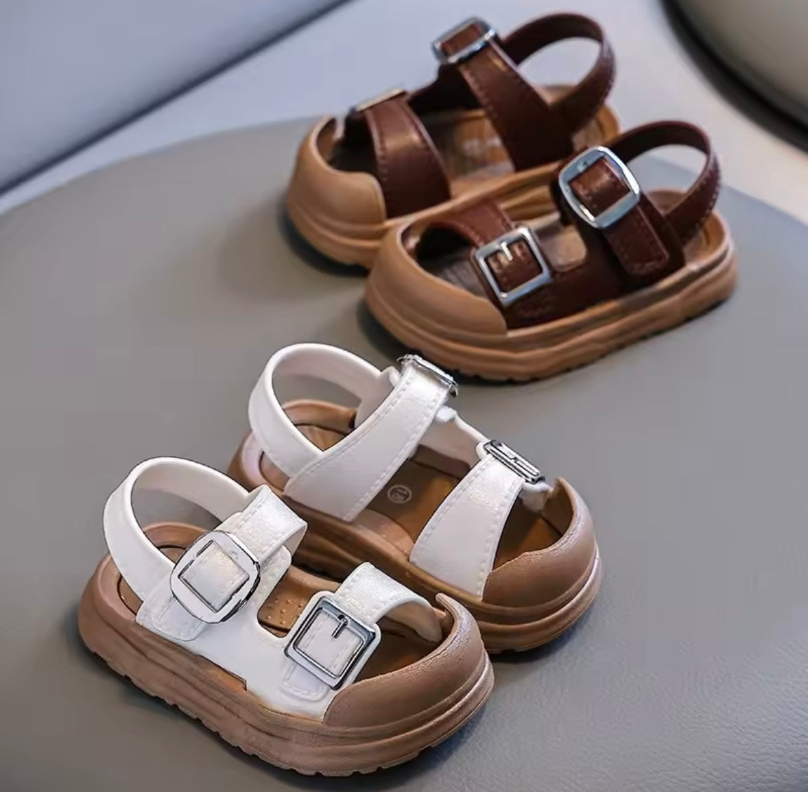 Pair of brown and white sandals with buckles on a gray surface