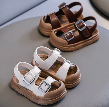 Pair of brown and white sandals with buckles on a gray surface