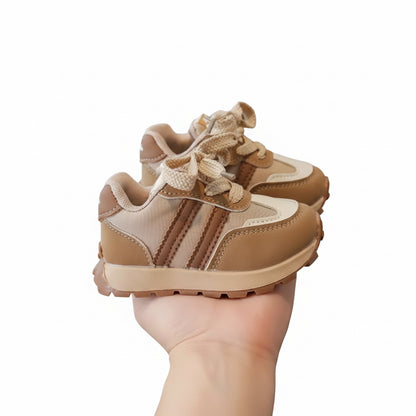 Pair of tan children's sneakers held in a hand with a blurred indoor background