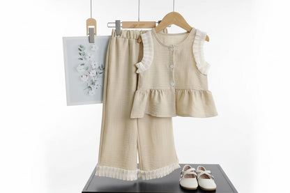Children's beige outfit with ruffled details on a hanger against a dark background.