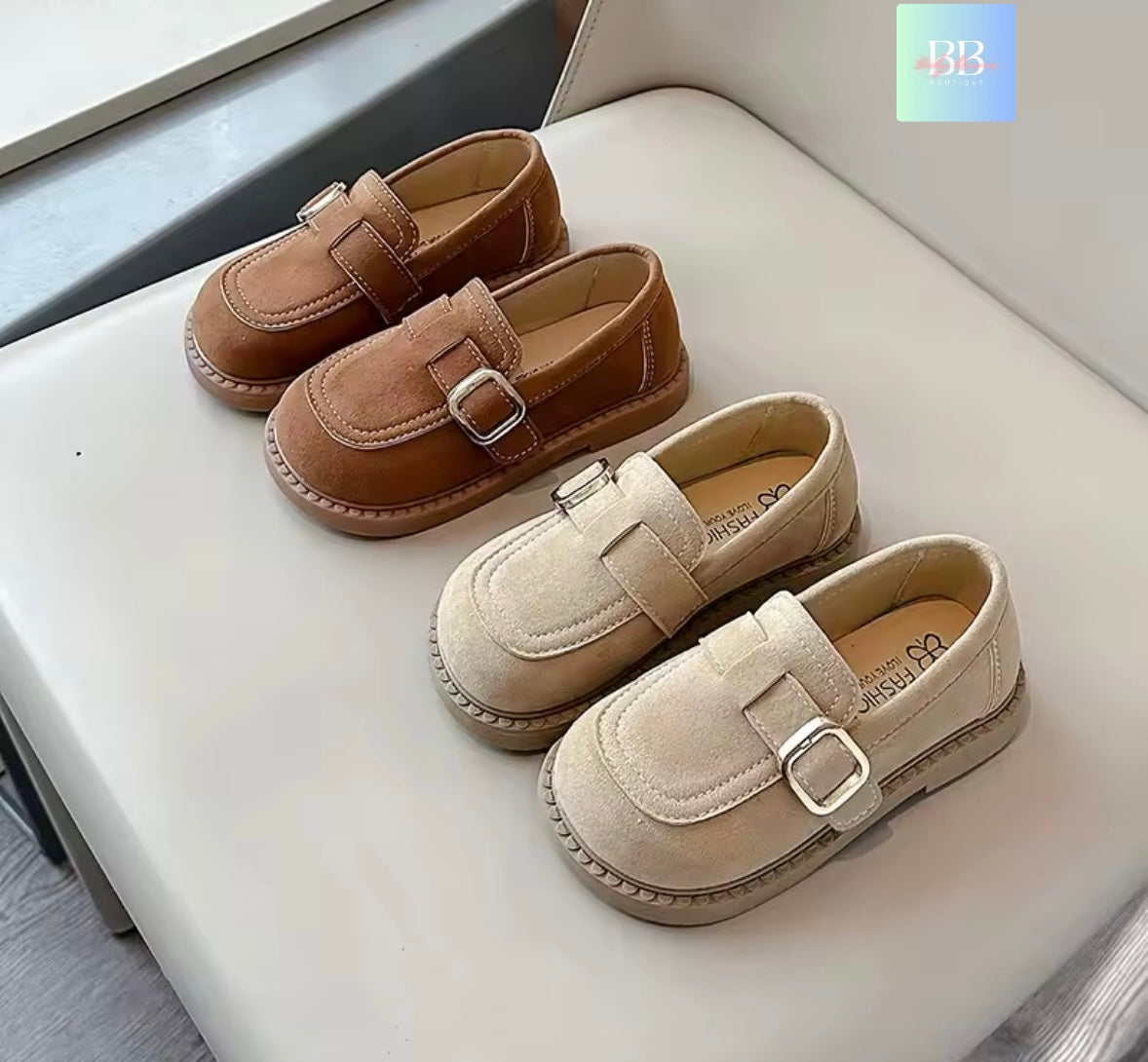 Pair of brown and beige loafers with buckles on a white surface.