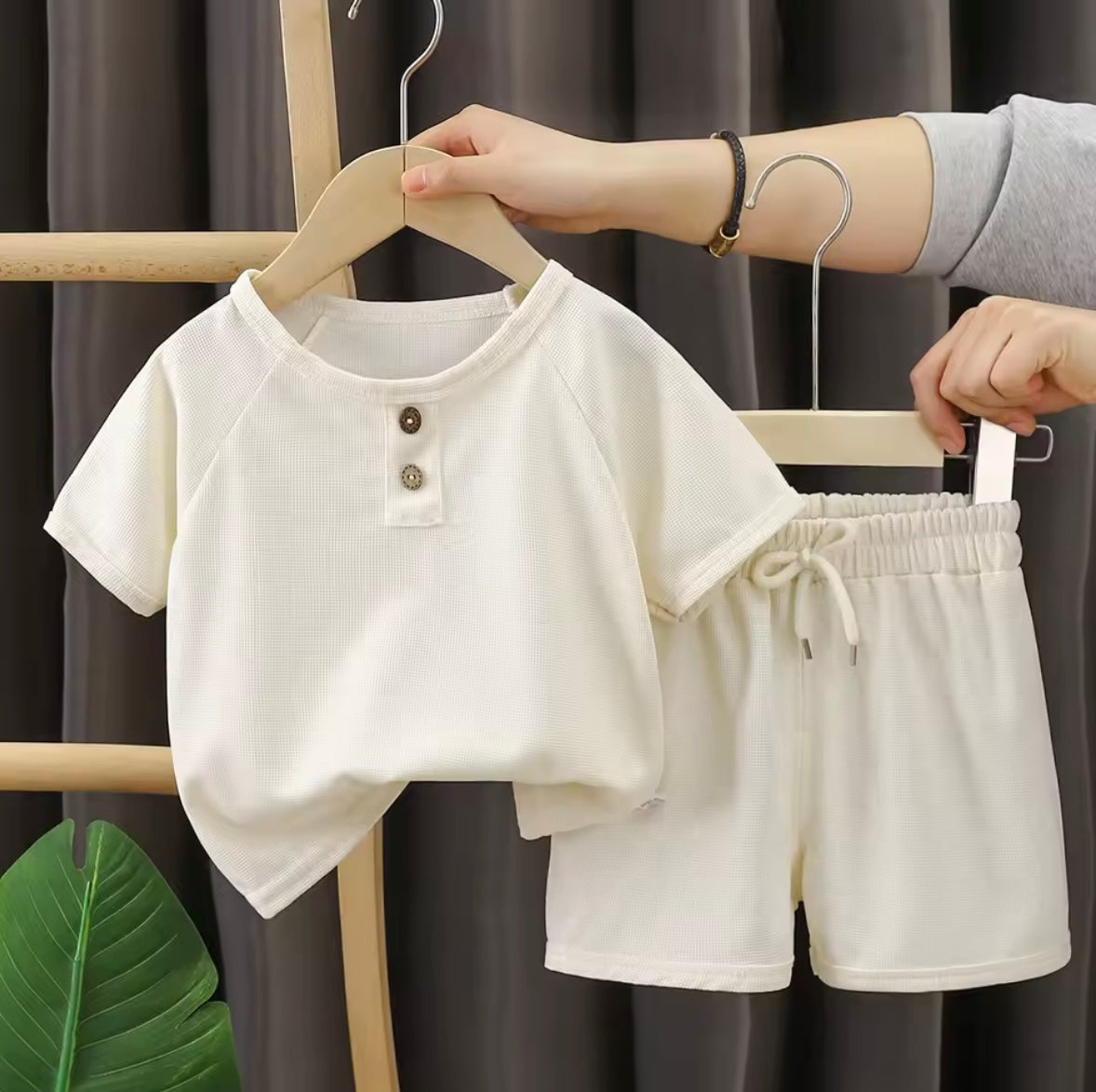 White children's outfit on hangers against a dark curtain background