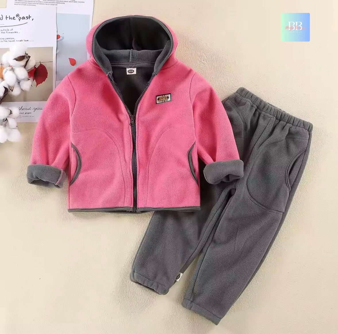 Children's pink and gray fleece jacket and pants set on a beige surface.