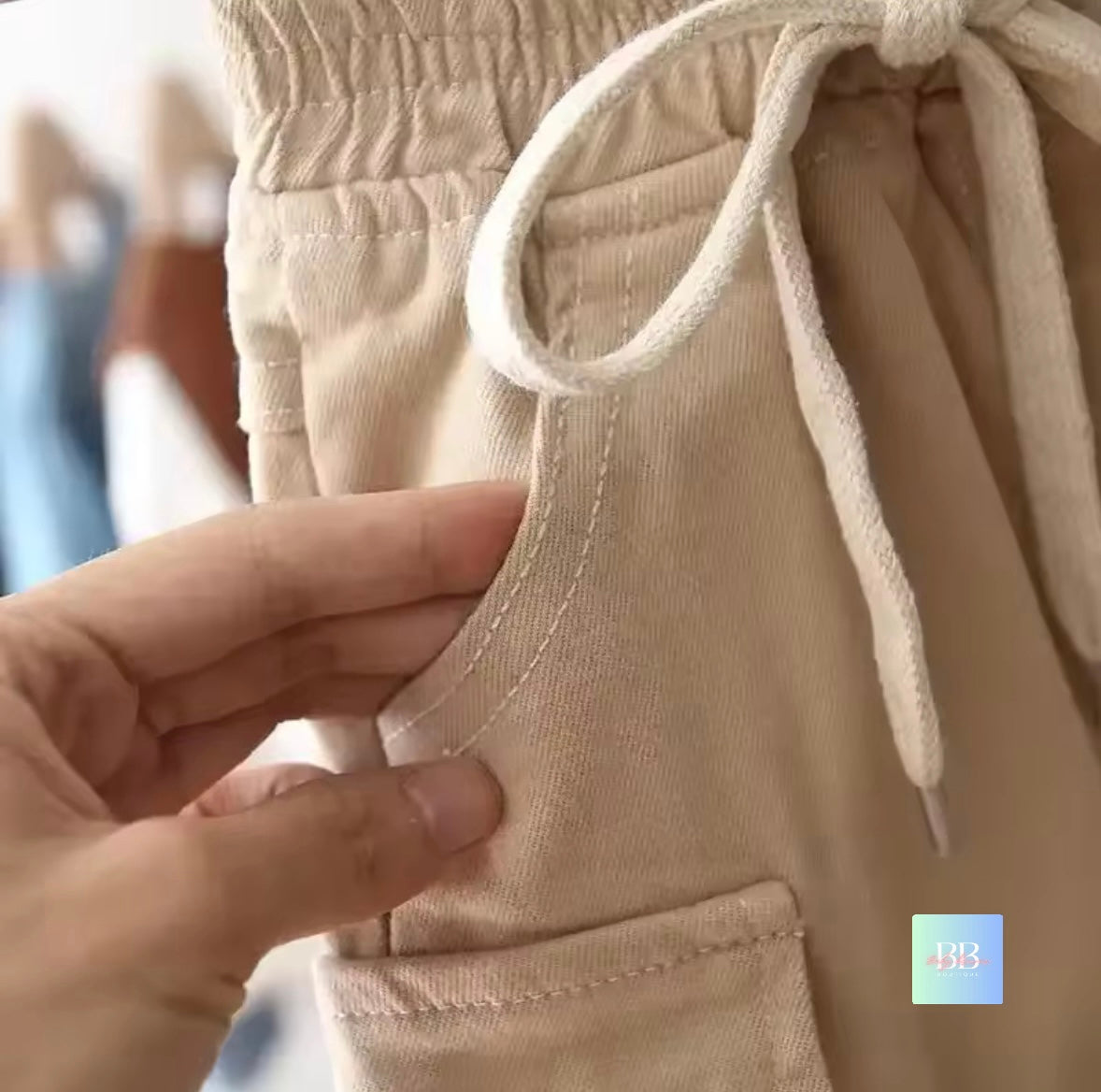 Close-up of beige pants with a hand adjusting the drawstring.