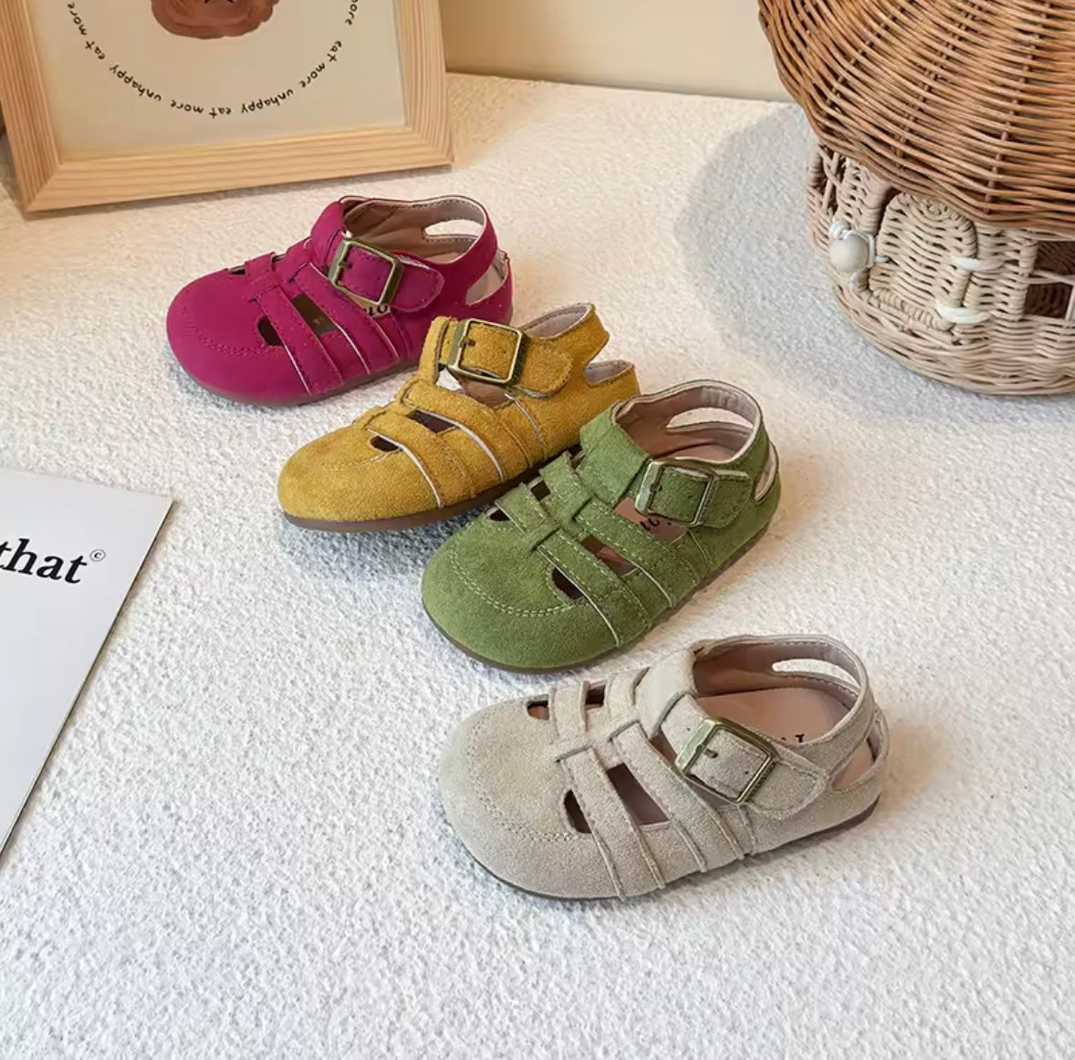 Four colorful children's sandals on a textured surface with a wicker basket in the background.