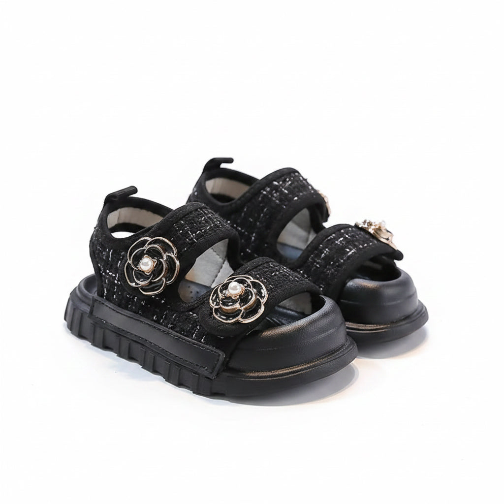 Black sandals with floral embellishments on a gray surface