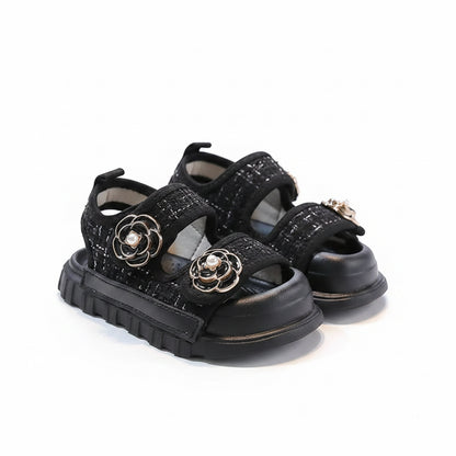 Black sandals with floral embellishments on a gray surface