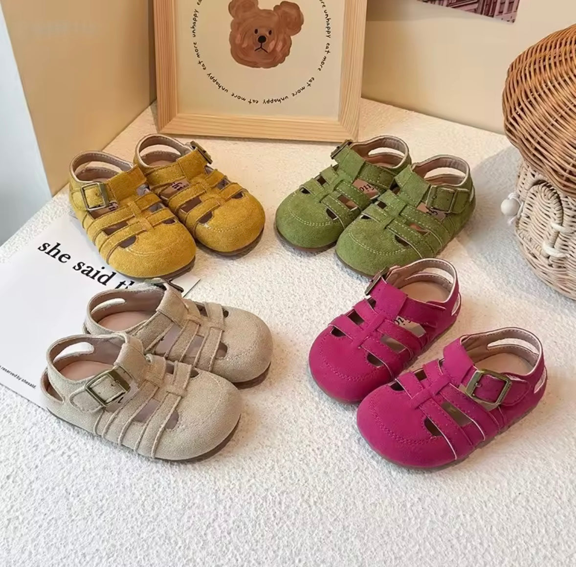 Set of colorful children's sandals on a textured surface with a framed picture in the background.