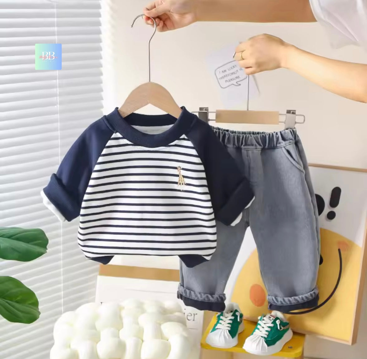 Children's outfit with striped shirt and gray pants on a hanger against a light background.