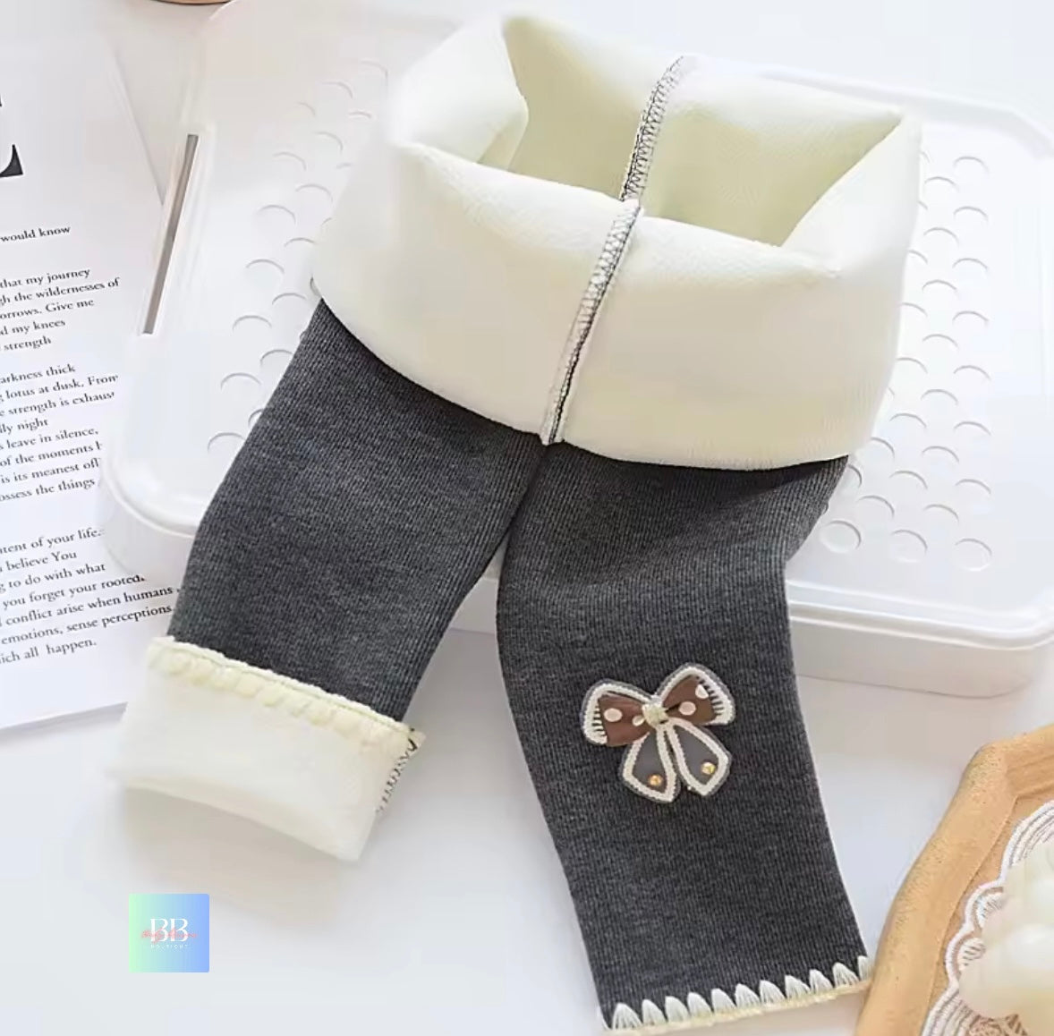 Gray leggings with a white waistband and a decorative bow on a light surface.