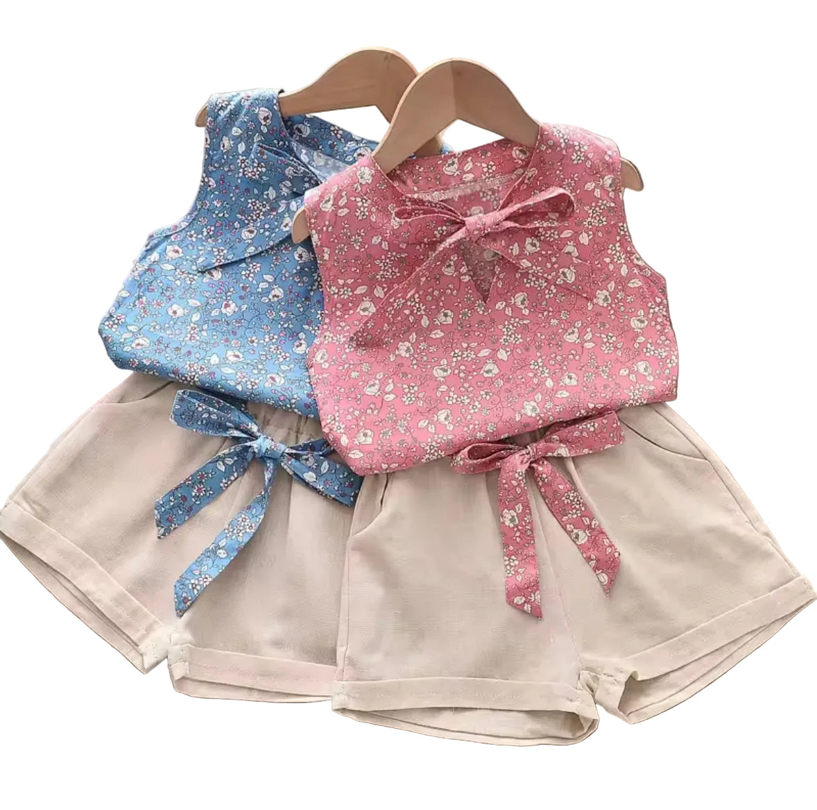 Two children's outfits with floral tops and shorts on hangers against a white background.