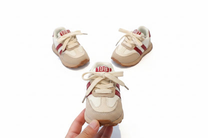 Pair of children's sneakers with red and white stripes on a gray surface.