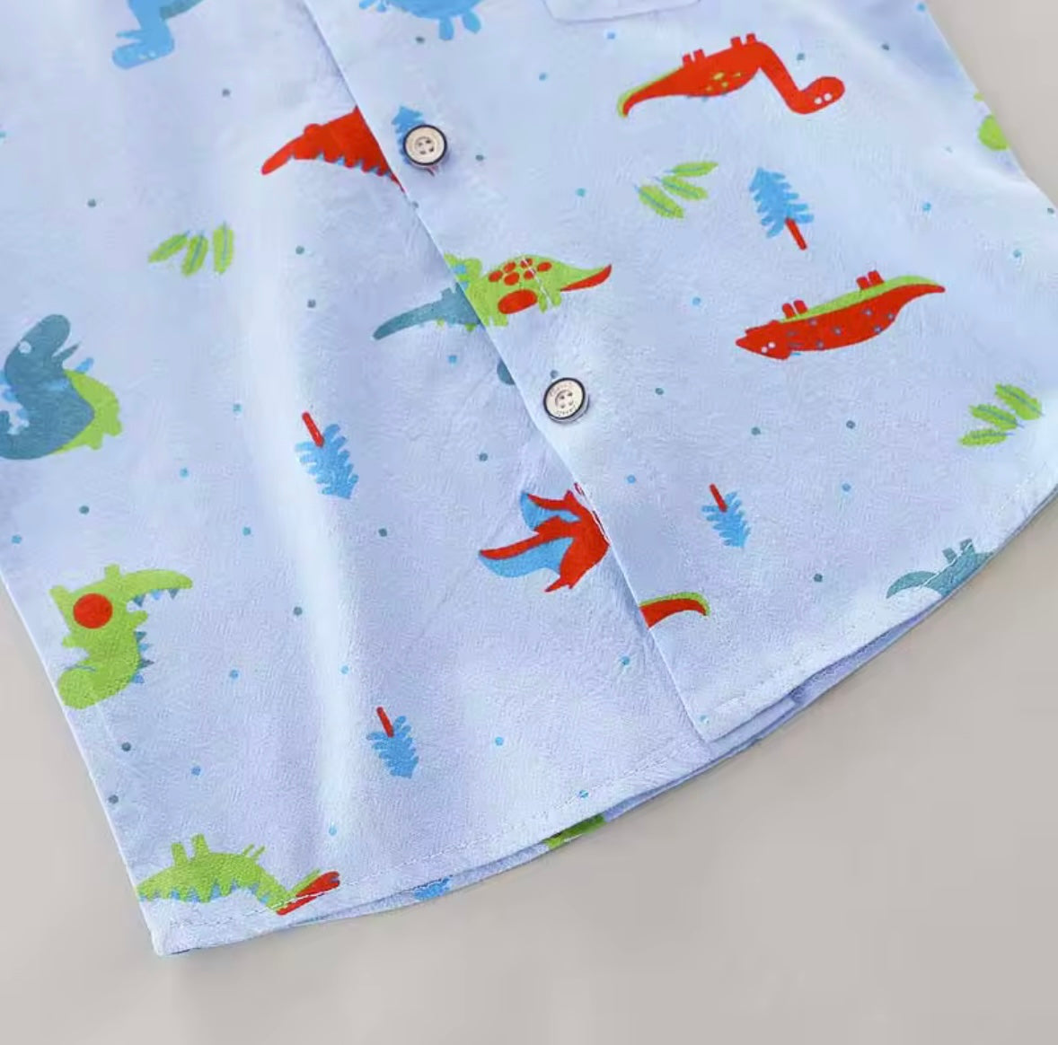 Two pieces of fabric with colorful dinosaur patterns on a light blue background.