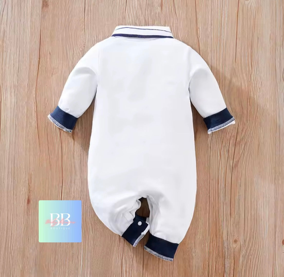 White baby romper with navy trim on a wooden surface, featuring a 'BB' card.