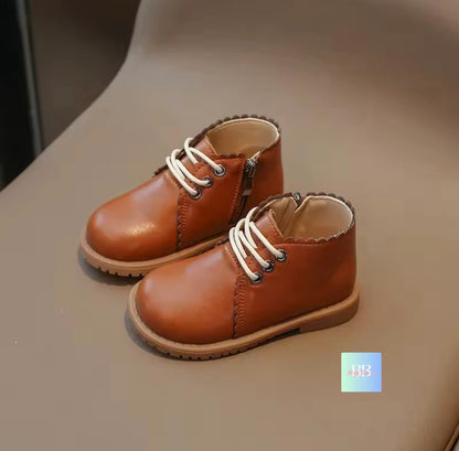 Pair of brown children's shoes with white laces on a beige surface