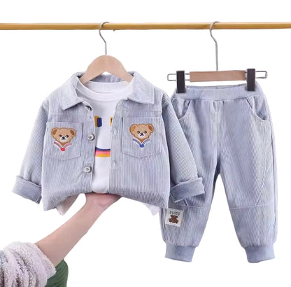 Children's clothing set with jacket, shirt, and pants on hangers against a gray curtain background.