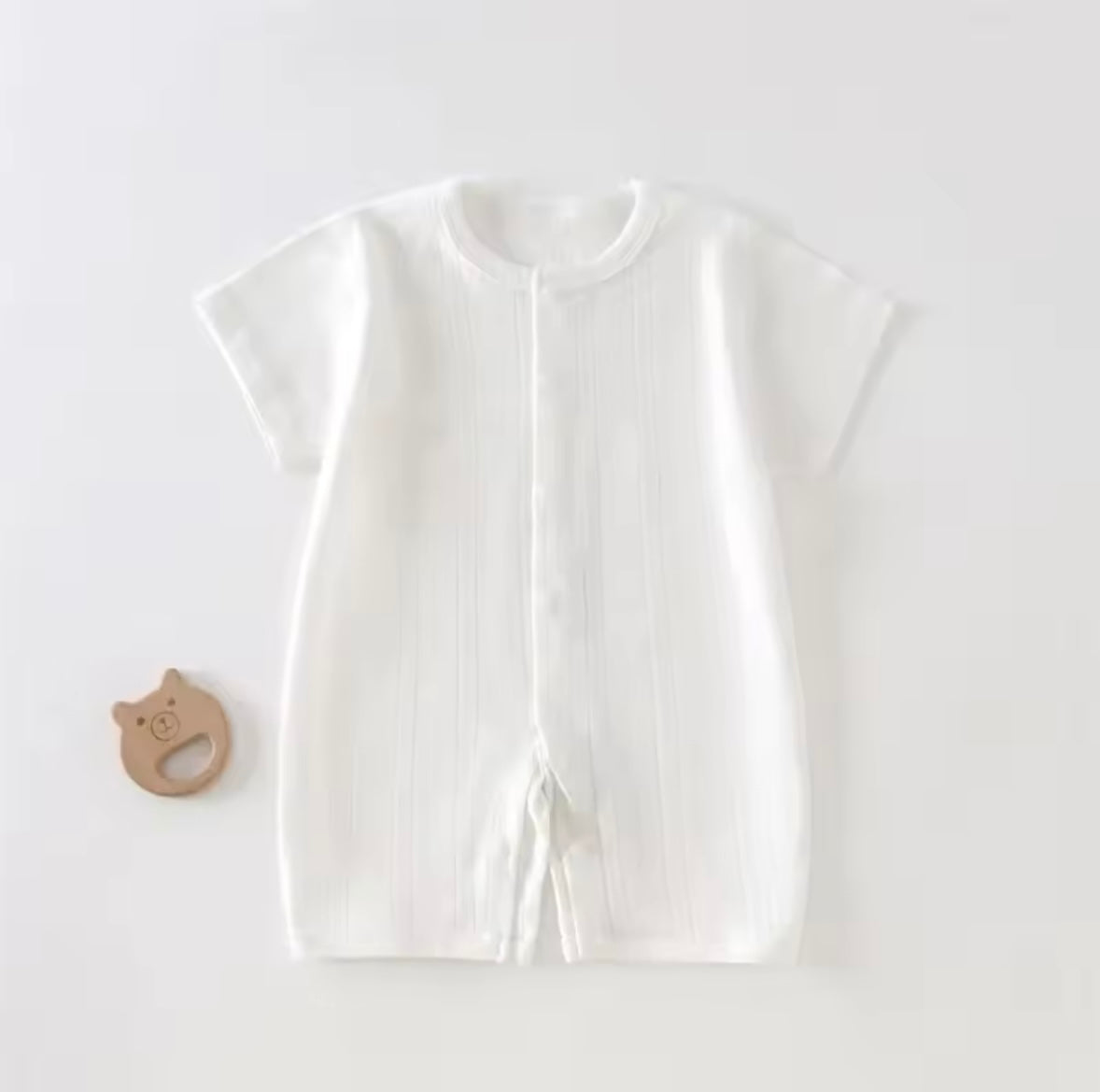 White baby outfit with a wooden teether on a light gray background