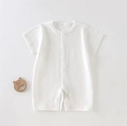 White baby outfit with a wooden teether on a light gray background