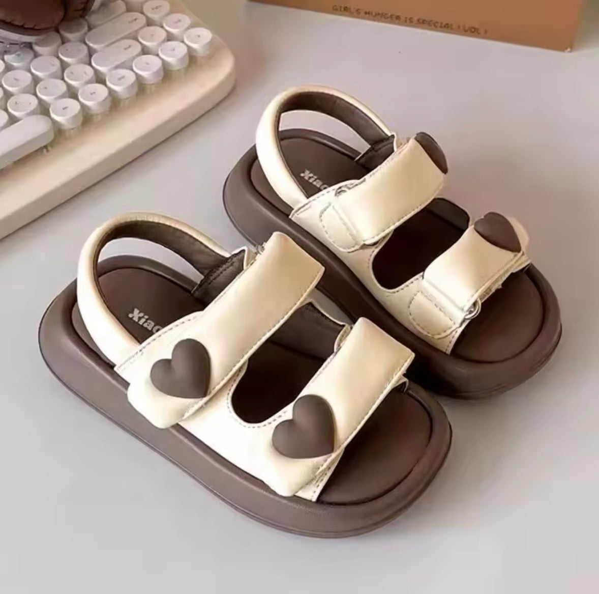 Pair of children's sandals with heart designs on a light surface.