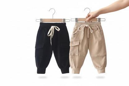 Two pairs of children's pants, one black and one beige, hanging on a rack.