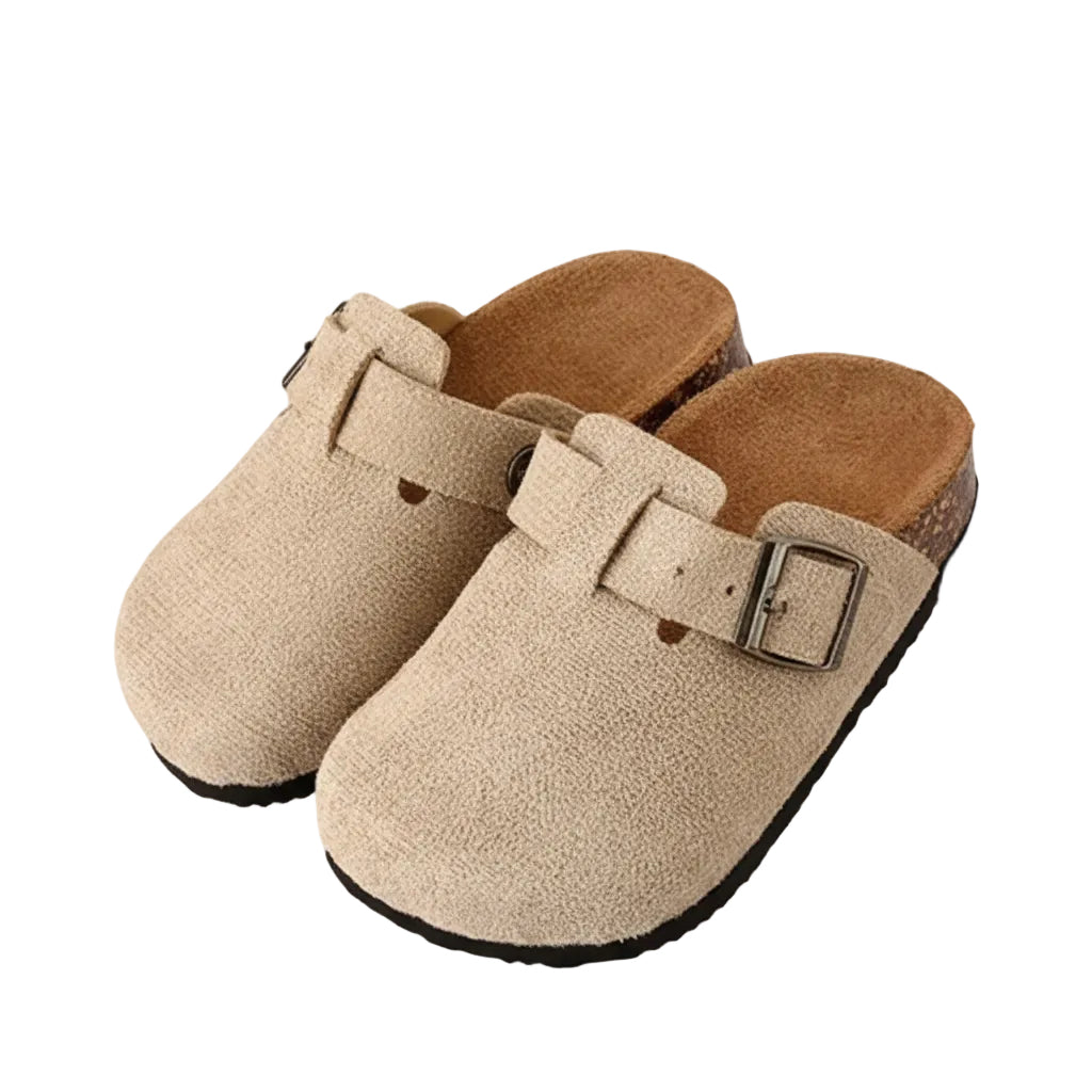 Pair of beige clogs with a buckle on a wooden shelf.