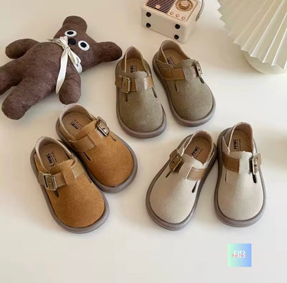Set of children's shoes in various colors on a white surface with a small brown teddy bear.