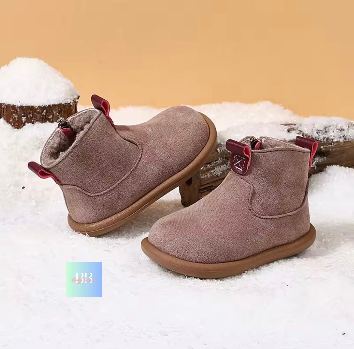 Pair of brown suede boots with red accents on a snowy background