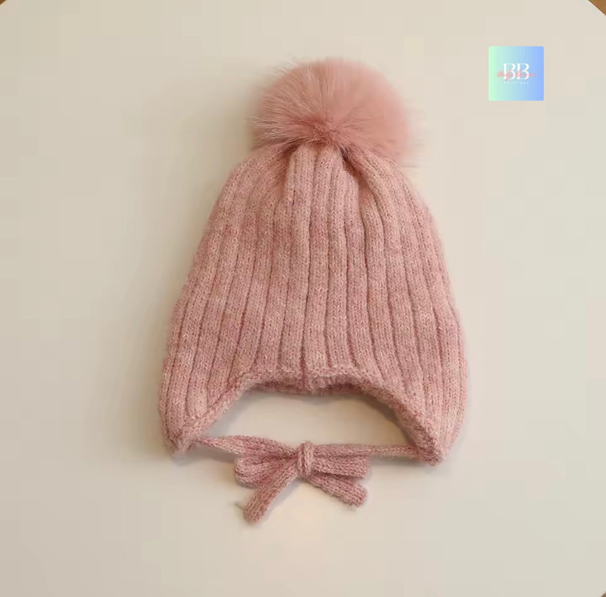 Pink knitted baby hat with a pom-pom on a light beige background
