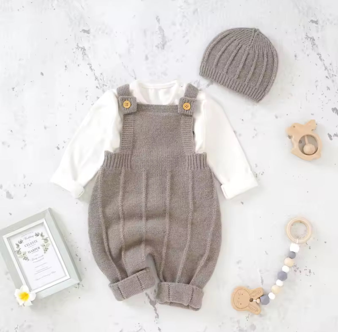 Knitted baby romper with matching hat on a light gray surface with toys around