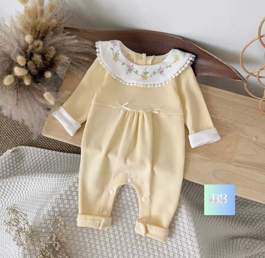 Beige baby romper with floral collar on a textured surface