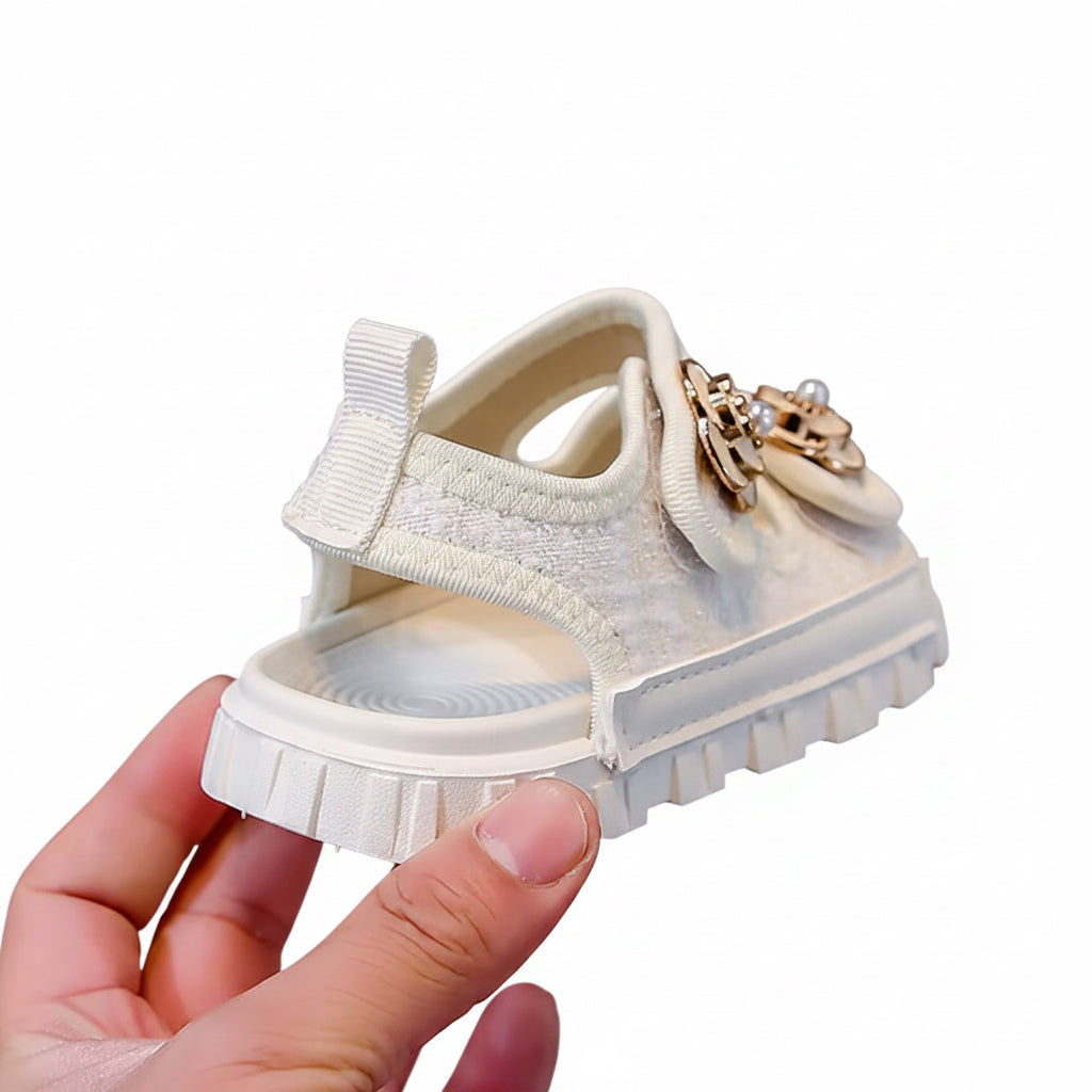 White sandal with decorative bow and charm held by a hand against a neutral background