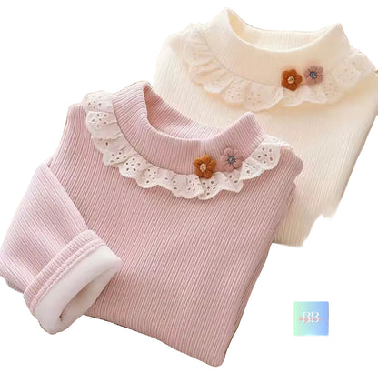 Two ribbed knit shirts with lace collars and floral details on a wooden surface.
