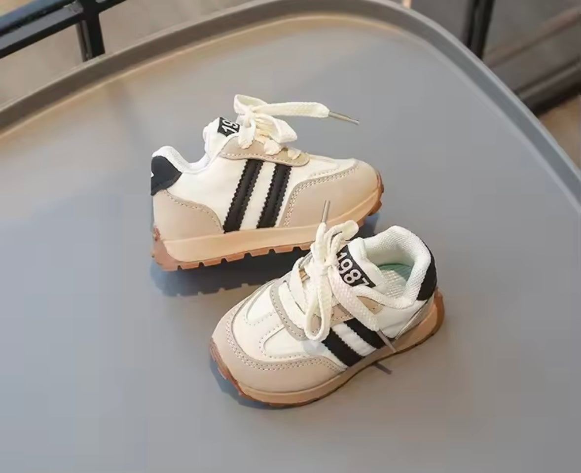 Pair of children's sneakers with black stripes on a gray surface